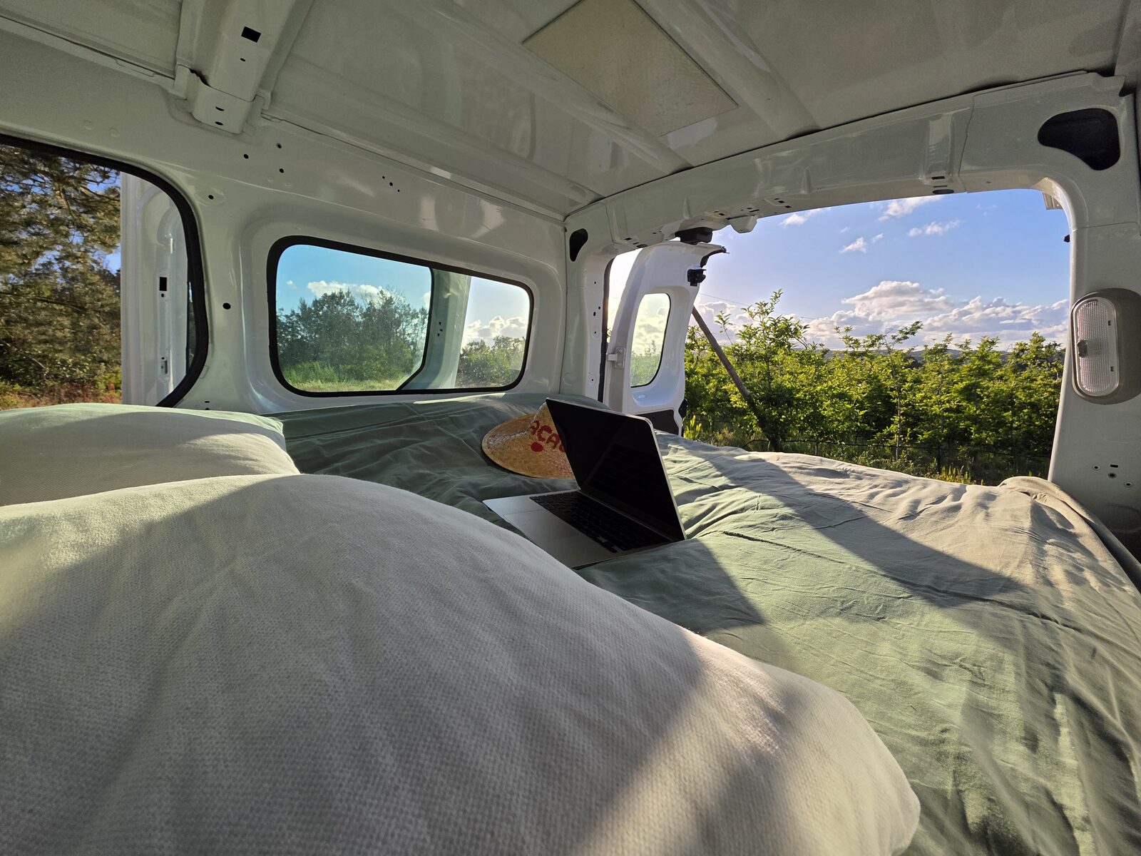 Laptop on the bed framed by open rear doors looking out over green countryside
