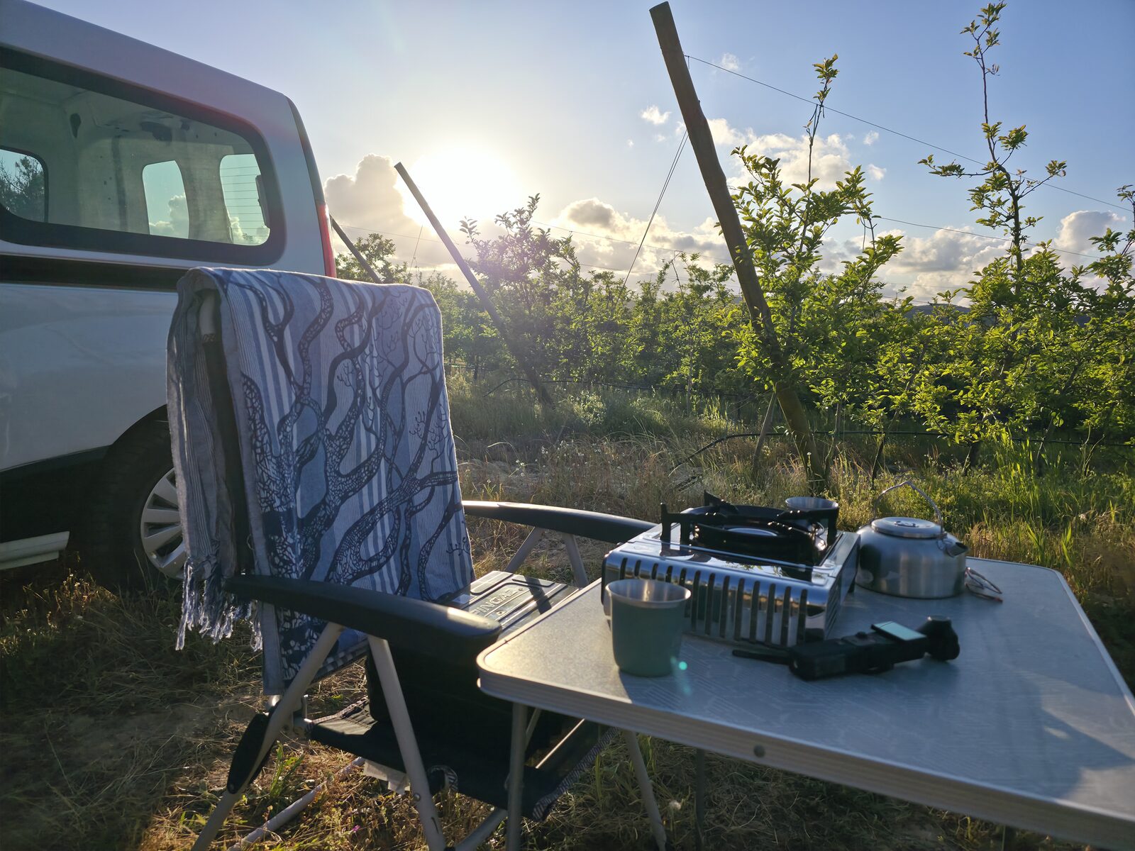 Gas stove and kettle on the camp table beside the van as the sun sets