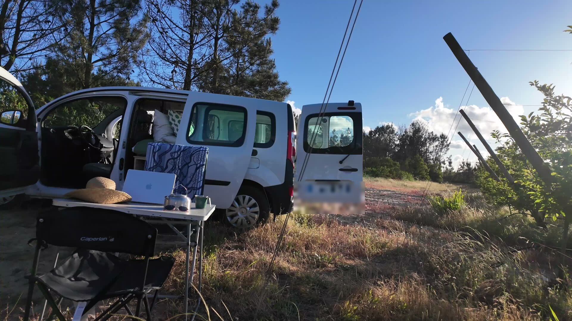 Camp set up beside the van at golden hour with table, chairs, laptop and straw hat