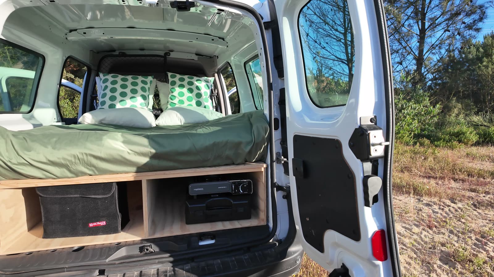 Rear doors open onto a made bed with storage drawers and a power station below