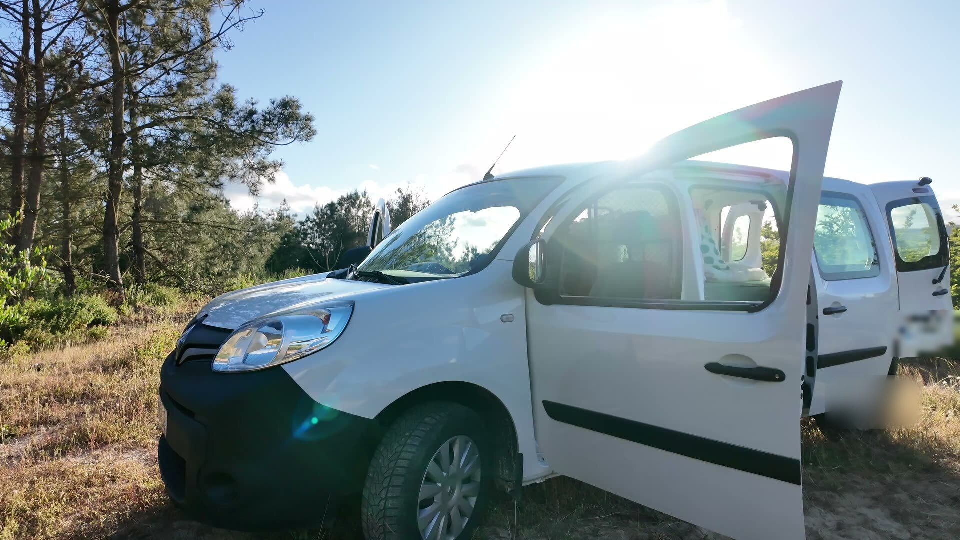 Front three-quarter view with doors open and sun flaring through the pines