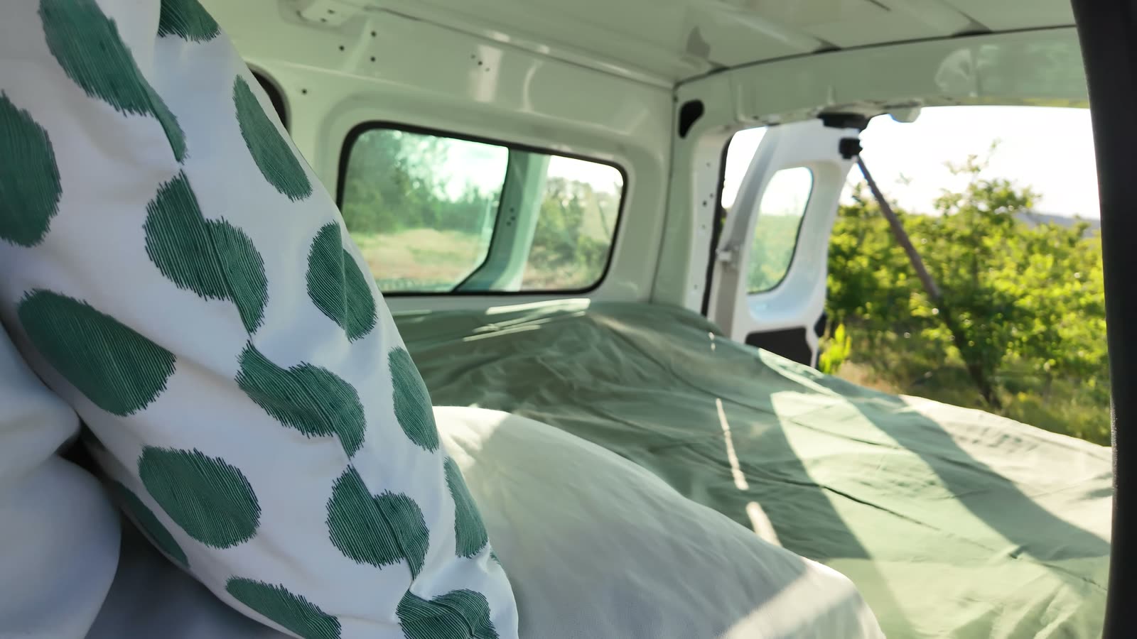 Cozy bed with green polka-dot pillow and warm evening sun through the windows