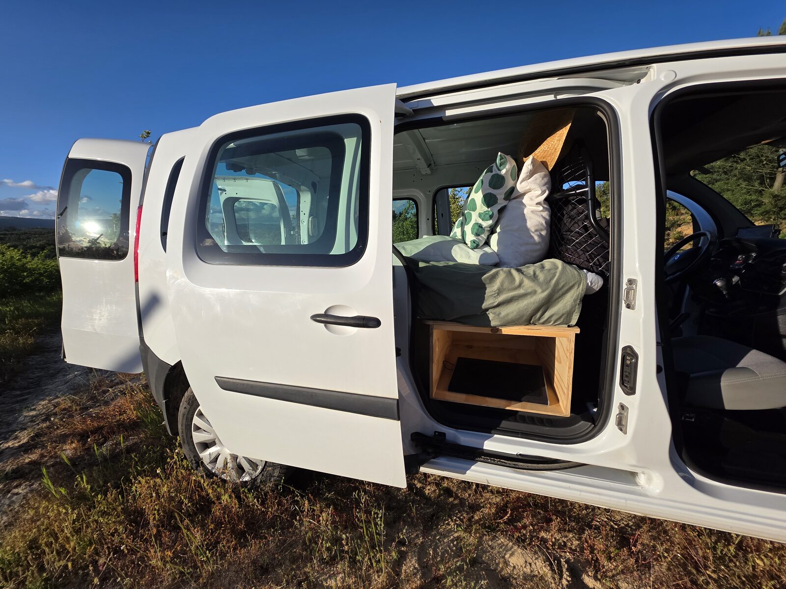 Sliding door open revealing the made-up bed inside, parked on a hilltop under blue sky